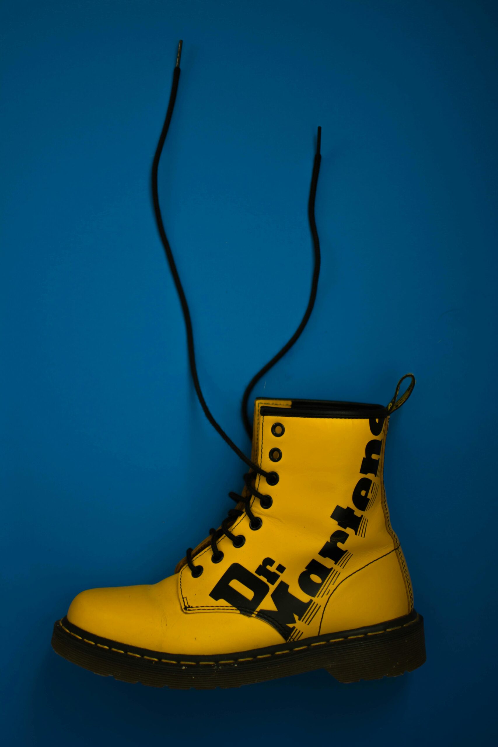 Bright yellow Dr. Martens boot designed for men shoes for everyday wear, featuring black laces and bold branding on a blue background