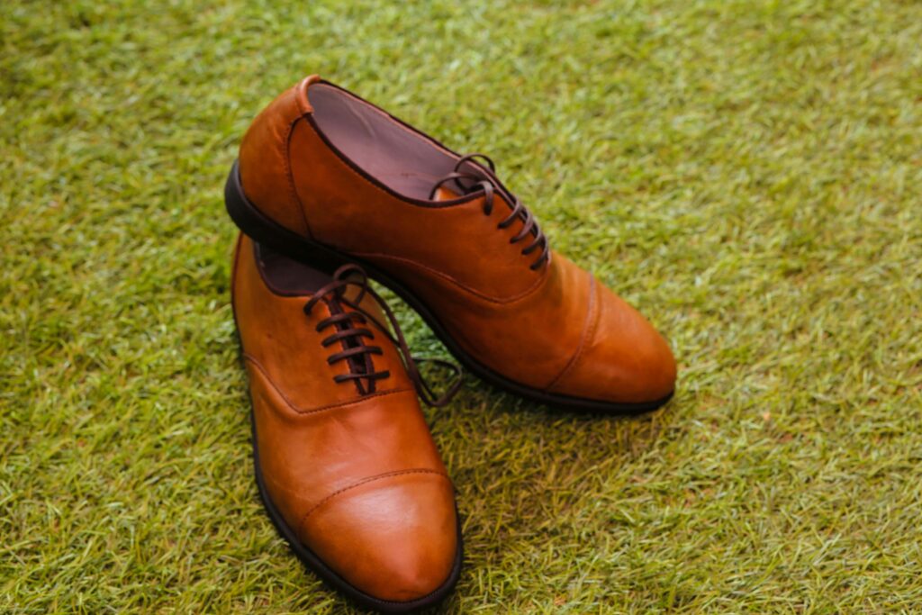"Elegant brown leather men shoes for everyday wear placed on green grass, perfect for casual and formal daily use.
