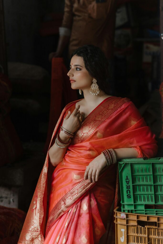 Elegant woman in a rich coral pink silk saree with golden embroidery, showcasing the saree collection for every occasion