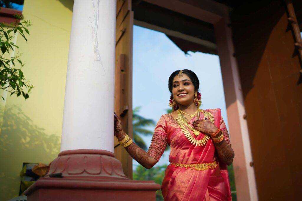 Smiling woman in a traditional pink silk saree with gold jewelry, representing a saree collection for every occasion